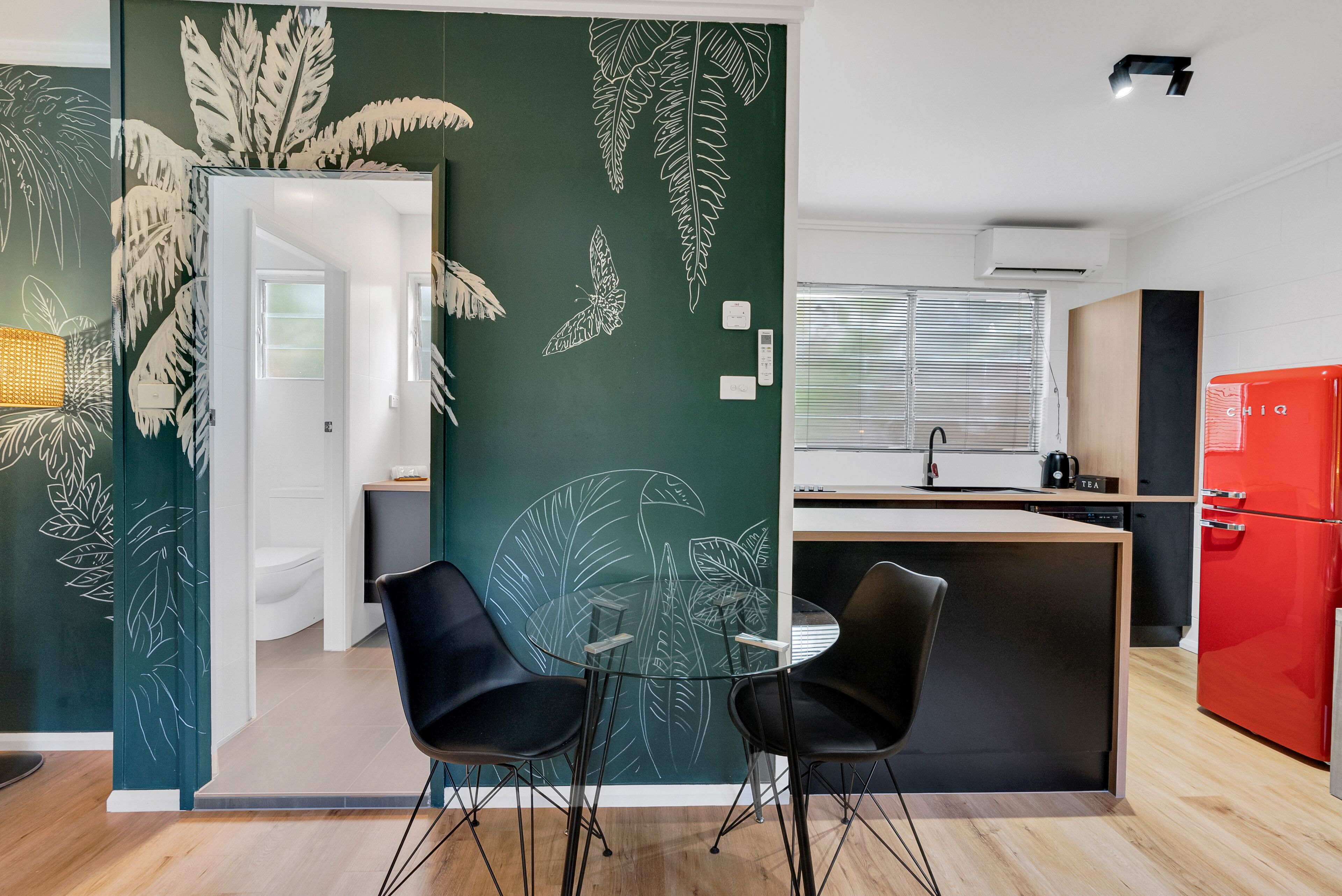 Een moderne keuken met een rode koelkast, twee zwarte stoelen en een glazen tafel.