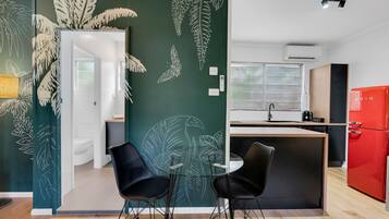 Een moderne keuken met een rode koelkast, twee zwarte stoelen en een glazen tafel.