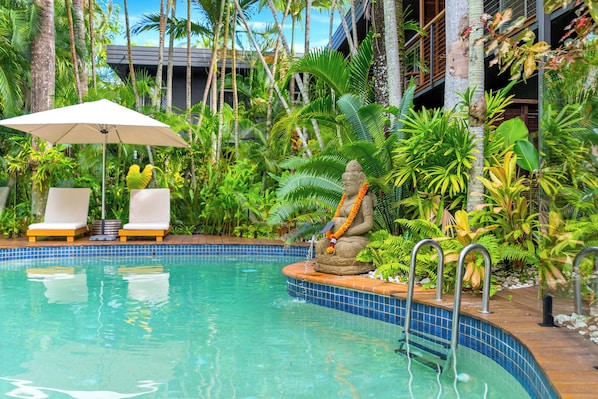 A pool with a statue, lounge chairs, and a tiled deck.