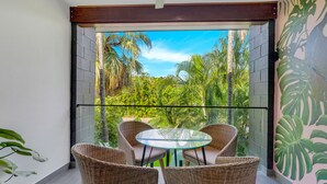A balcony with wicker chairs and a glass table, overlooking a lush garden. - The Palms at Palm Cove (Palm Cove)