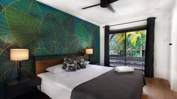 A bedroom with a large bed, two bedside tables with lamps, a ceiling fan, and a window with a view of greenery.