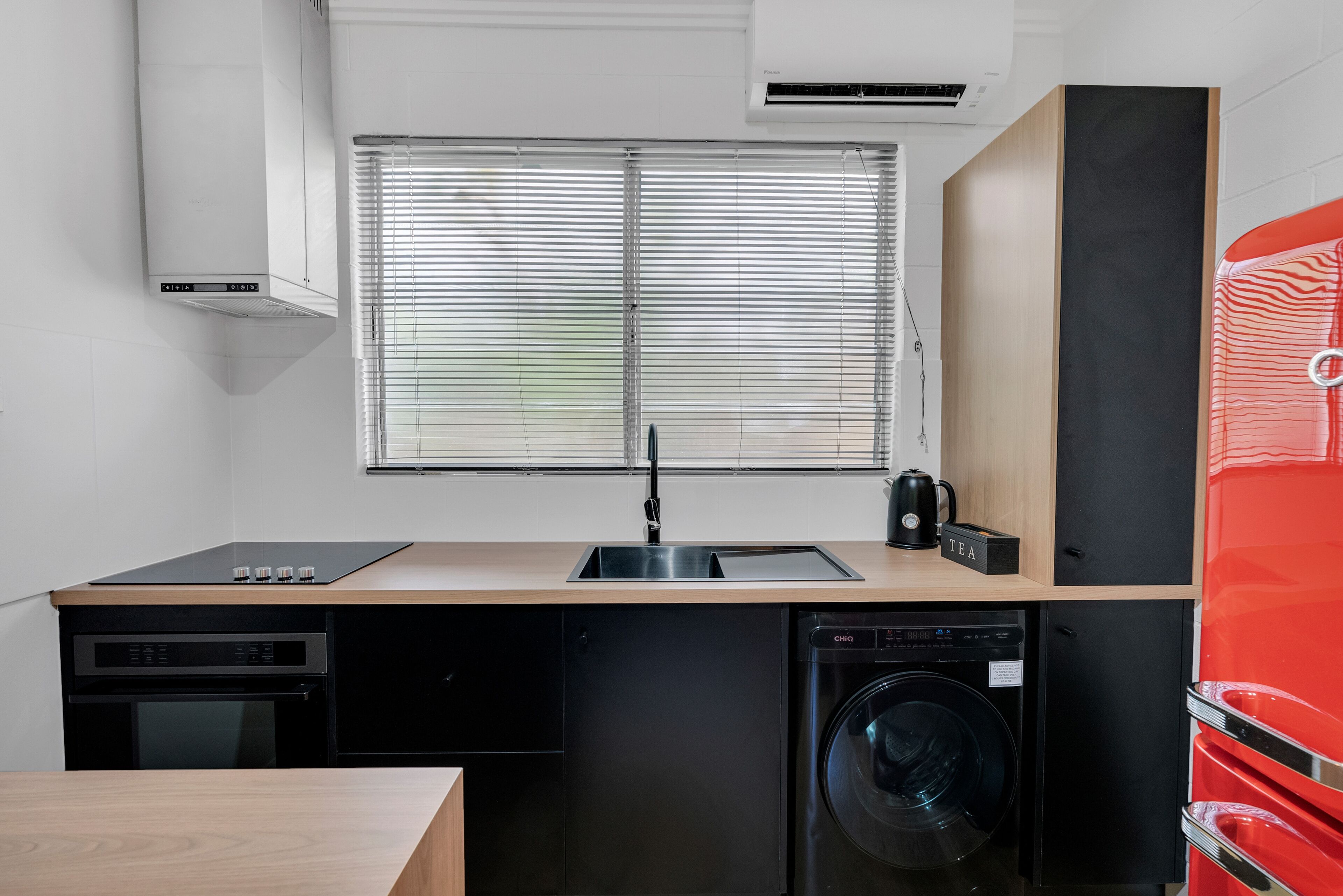 A compact kitchen with a sink, a dishwasher, a washing machine, and a red appliance.