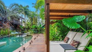 A wooden deck leading to a pool with lounge chairs and a pergola. - The Palms at Palm Cove (Palm Cove)