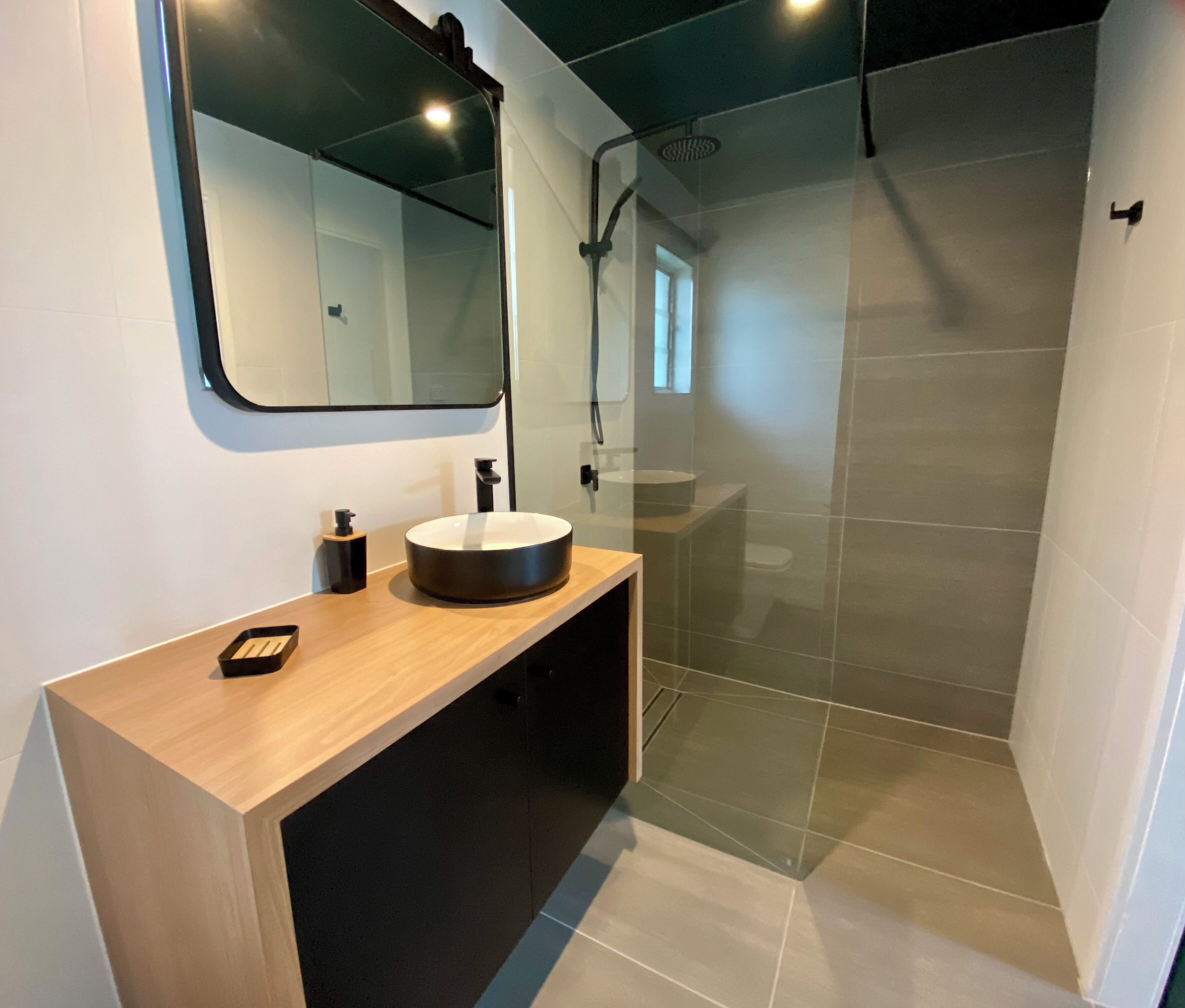A modern bathroom with a wooden vanity, a round sink, and a glass shower enclosure.
