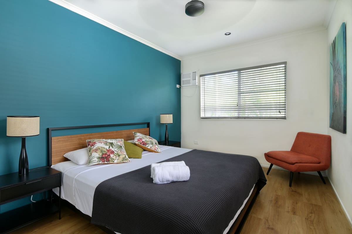 A hotel room with a bed, a desk, a chair, and a window with blinds.