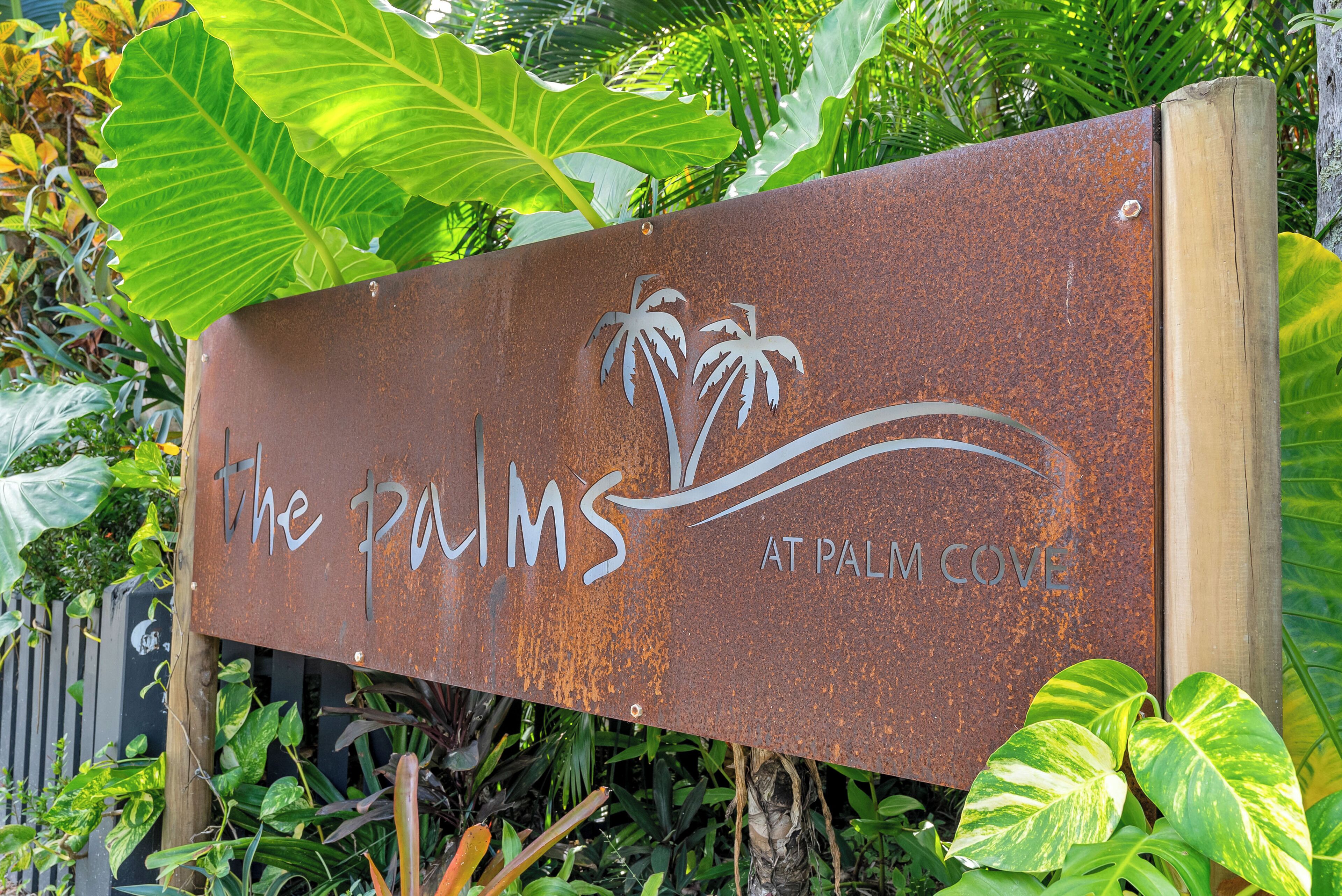 A rusty sign with "The Palms at Palm Cove" written on it.