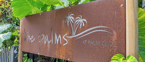 A rusty sign with "The Palms at Palm Cove" written on it.
