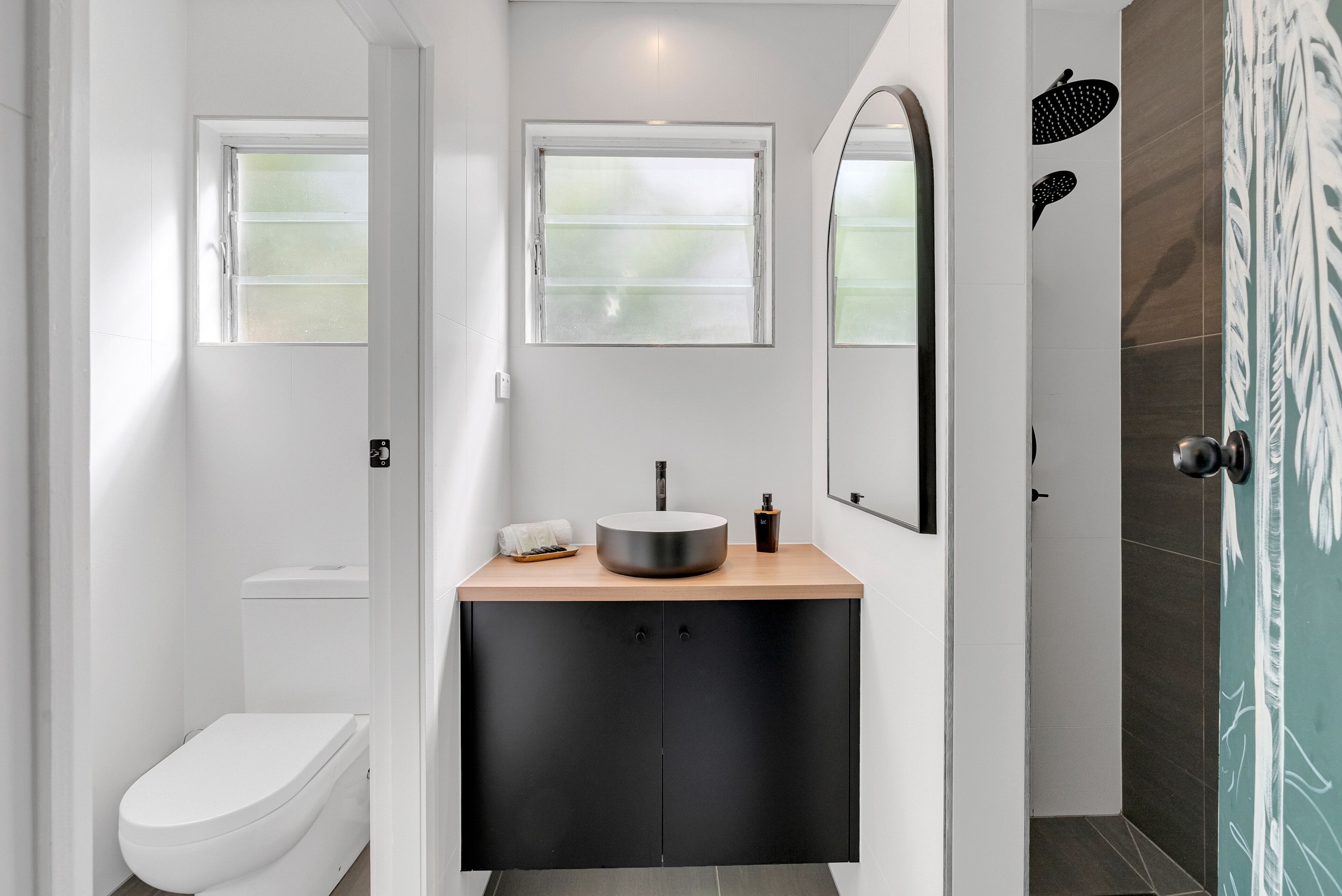 A modern bathroom with a white toilet, a round sink, and a shower area.