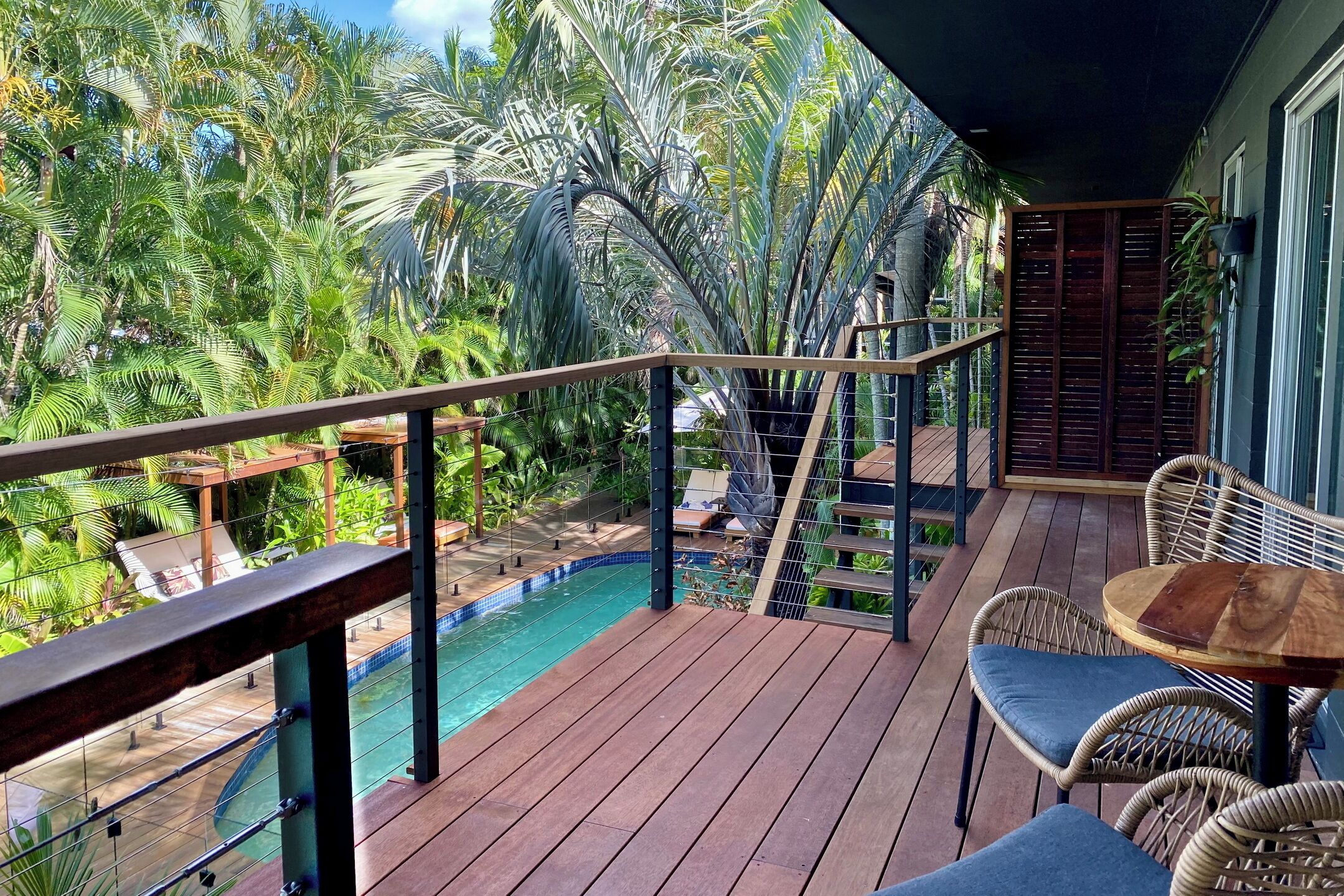 Una terraza de madera con piscina, rodeada de exuberante vegetación tropical.