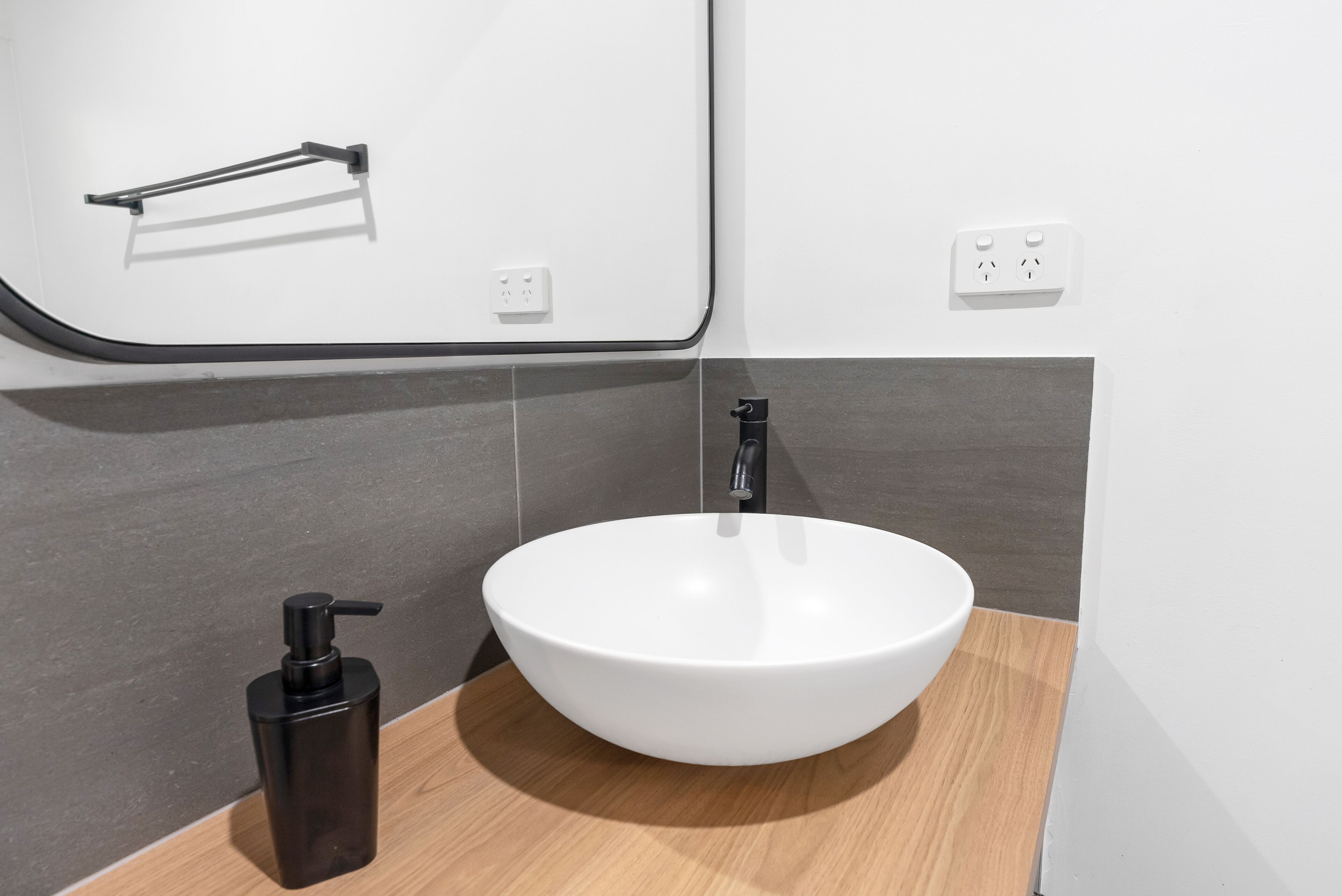 Un bagno moderno con un lavandino bianco, un rubinetto nero e un dispenser per sapone nero.