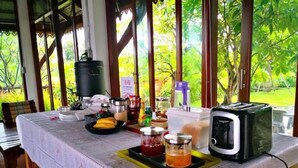 A breakfast table with a toaster, jars of jam, a fruit tray, and a coffee maker. - Khum Nakhon Hotel (Nakhon Si Thammarat)