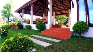 A covered outdoor area with steps leading to a building entrance, surrounded by well-maintained greenery and a clear sky. - Khum Nakhon Hotel (Nakhon Si Thammarat)