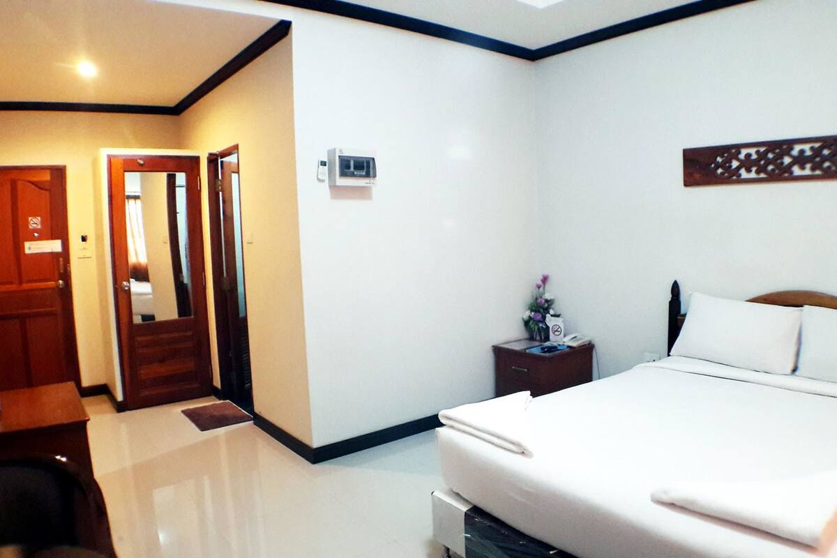 A hotel room with a bed, bedside table, nightstand, and a door leading to another room.