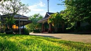 A grassy area with a building that has a covered patio and a visible entrance. - Khum Nakhon Hotel (Nakhon Si Thammarat)