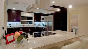 A modern kitchen with dark cabinetry, stainless steel appliances, and a granite countertop. - Summertime - Direct River and Gulf Access (Fort Myers)