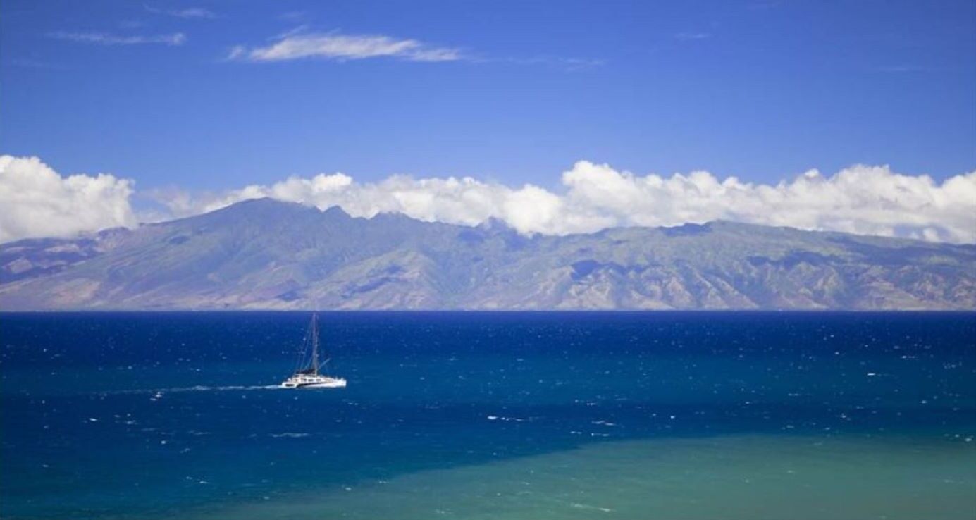 A boat sailing on a calm sea with a mountain range in the background.