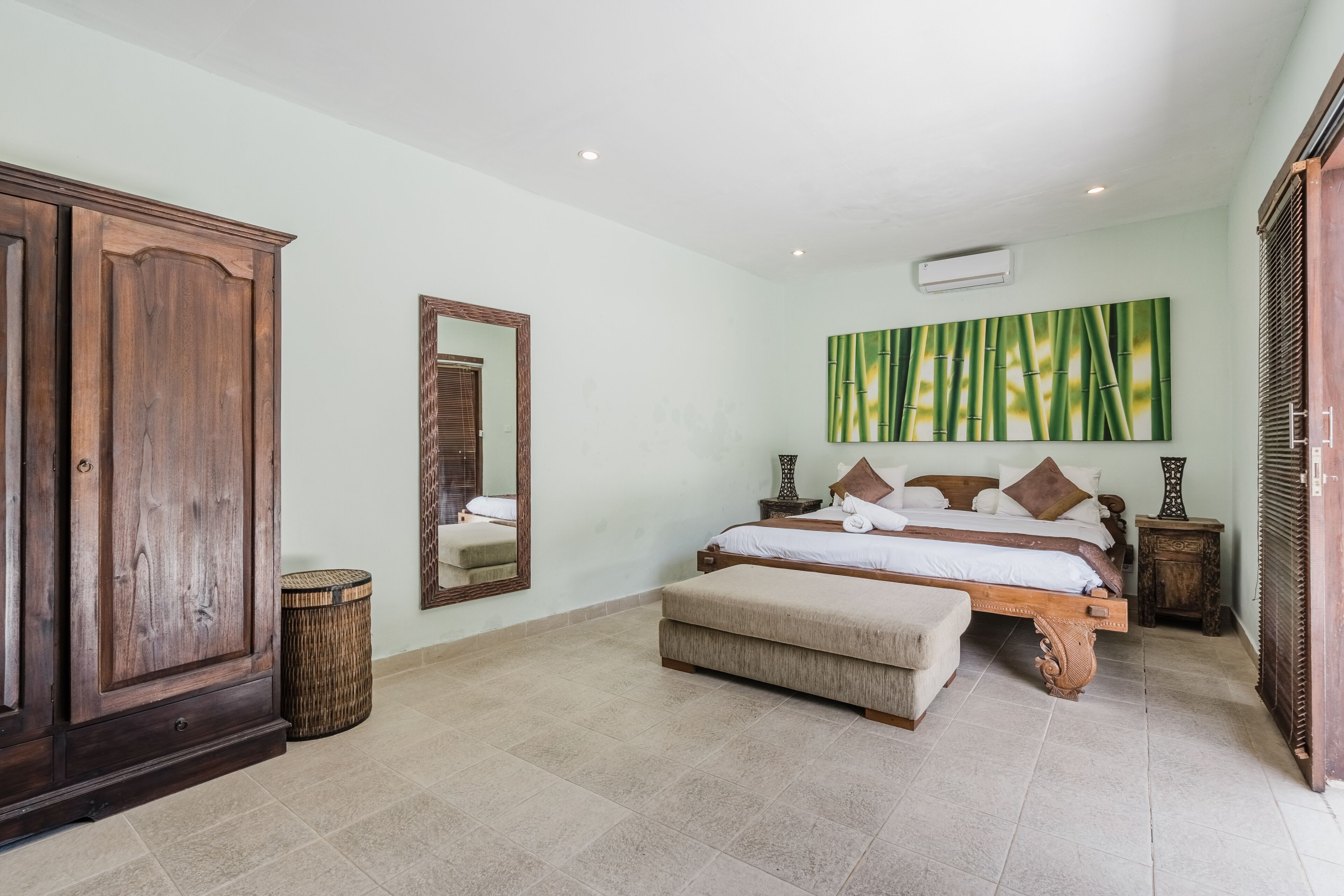 Un dormitorio con un armario grande de madera, una cama con estructura de madera, un banco y un espejo en la pared.