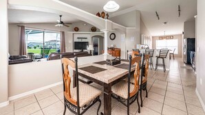 A spacious living area with a dining table, chairs, a TV, and a kitchen in the background. - Premier Host-Beautiful 4BR/2BA Pool HEAT Home SAFE QUIET Lot - Disney 15 Minutes (Kissimmee)