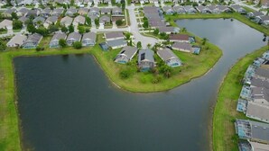 An aerial view of a residential area with houses, a central pond, and a small island with a house. - Premier Host-Beautiful 4BR/2BA Pool HEAT Home SAFE QUIET Lot - Disney 15 Minutes (Kissimmee)