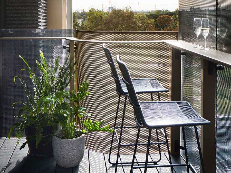Un balcón con una mesa y sillas, una planta en maceta y dos copas de vino.