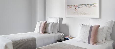 Une chambre d’hôtel avec deux lits, du linge de lit blanc et un tableau représentant une scène de plage accroché au mur.