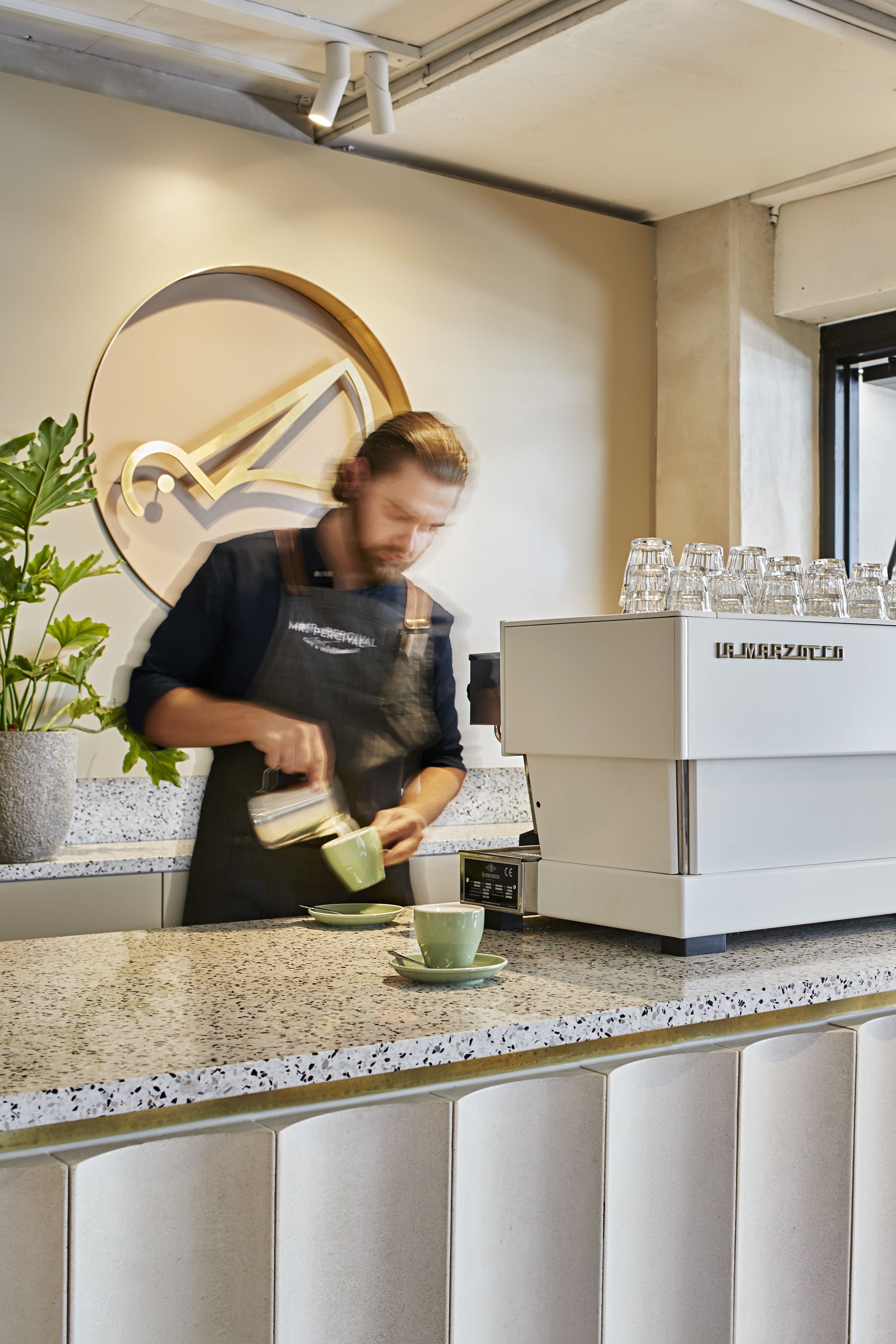 Een barista maakt koffie achter de bar, met een koffieapparaat en een decoratieve muur.