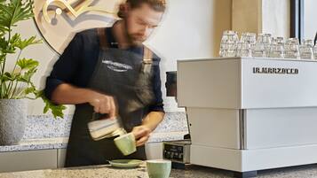 Een barista maakt koffie achter de bar, met een koffieapparaat en een decoratieve muur.