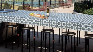 Une terrasse sur le toit avec une table carrelée aux motifs bleus et blancs, des chaises rouges et une vue sur l’océan.