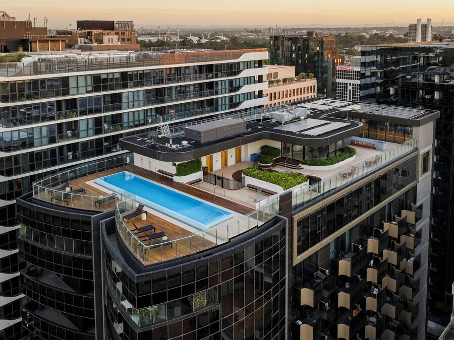 A high-rise building with a rooftop pool, multiple balconies, and a glass facade.