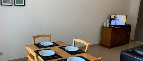 Ein Essbereich mit einem Holztisch, gedeckt für vier Personen, einem Fernseher auf einem Schrank und gerahmten Bildern an der Wand.