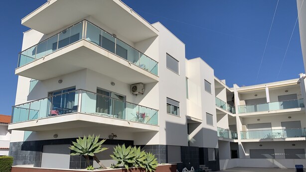 A modern multi-story residential building with balconies, a swimming pool, and a landscaped area with plants. - Sand House, New Apartment (Albufeira)