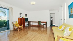 A spacious living area with a wooden floor, a yellow sofa, a wooden dining table with chairs, a television, and a framed picture on the wall. - Kiltevna (Maslin Beach)