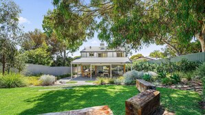 A two-story house with a covered patio, surrounded by a well-maintained garden and trees. - Port of Call (Port Willunga)