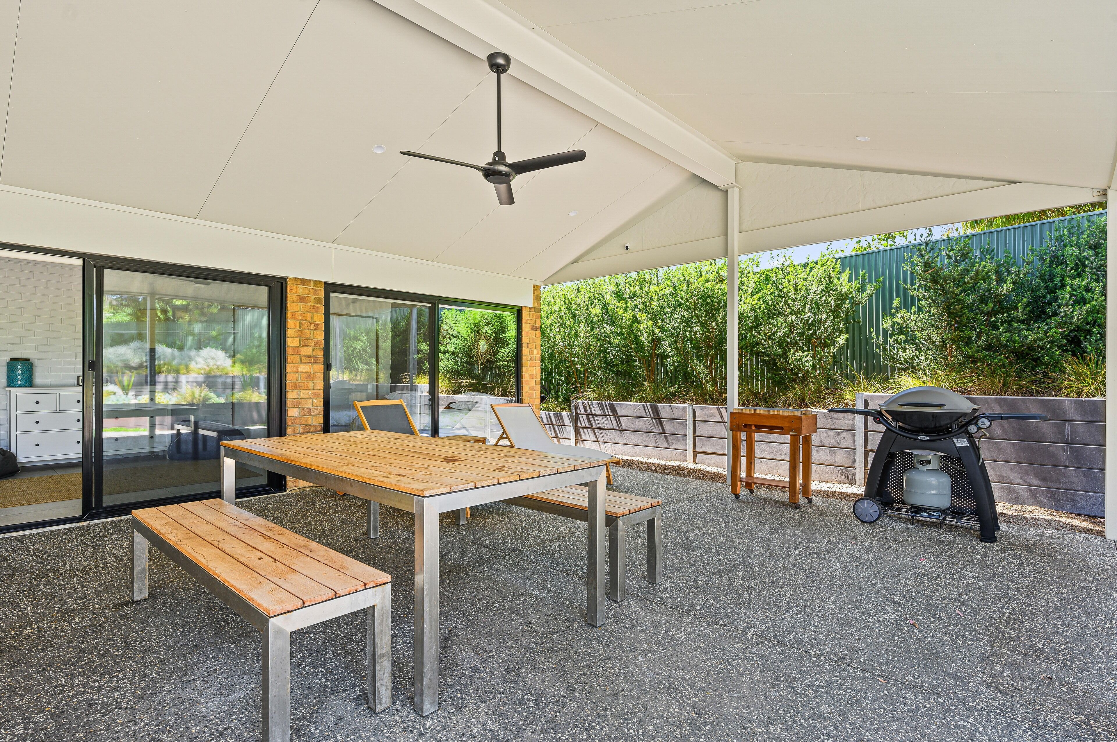 An outdoor patio with a table and benches, a ceiling fan, and a barbecue grill.