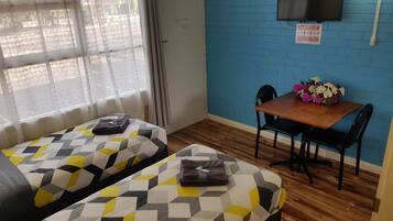 Una habitación con dos camas, una mesa de madera con sillas y un televisor montado en la pared.