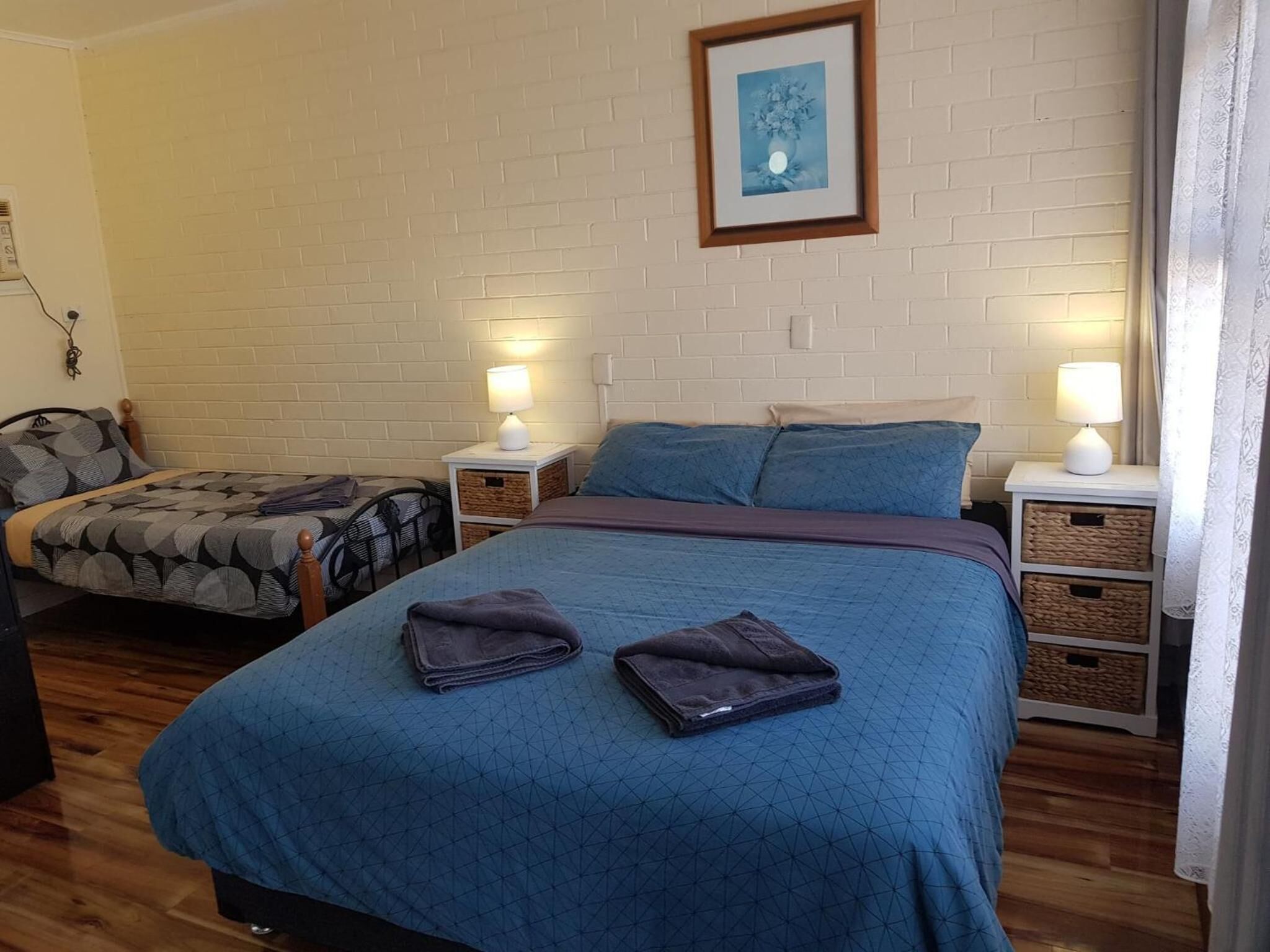 Habitación de hotel con dos camas, una pared de ladrillo, un cuadro enmarco y lámparas de noche.