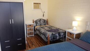A compact bedroom with a bed, a wardrobe, a bedside table, a lamp, and a wall-mounted air conditioner.