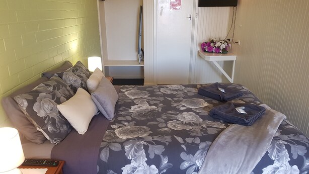 A neatly made bed with floral bedding, a bedside lamp, and a small table with a flower arrangement.