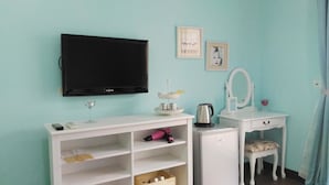 Une pièce comprenant une télévision, un bureau blanc avec un miroir, une petite armoire et une chaise.