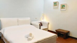 A hotel room with a bed, a chair, a small table, and two framed pictures on the wall. - MiNaMi Inn Kenting (Hengchun)