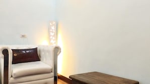Une pièce avec un fauteuil blanc, un banc en bois et un luminaire fixé au mur.