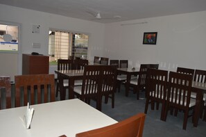 A conference room with multiple tables and chairs, a ceiling fan, and a window with blinds. - SAP Golden Grande (Anekal)
