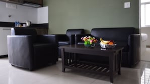 Una sala de estar moderna con una mesa de centro de madera oscura, dos sofás de cuero negro y una cocina al fondo.