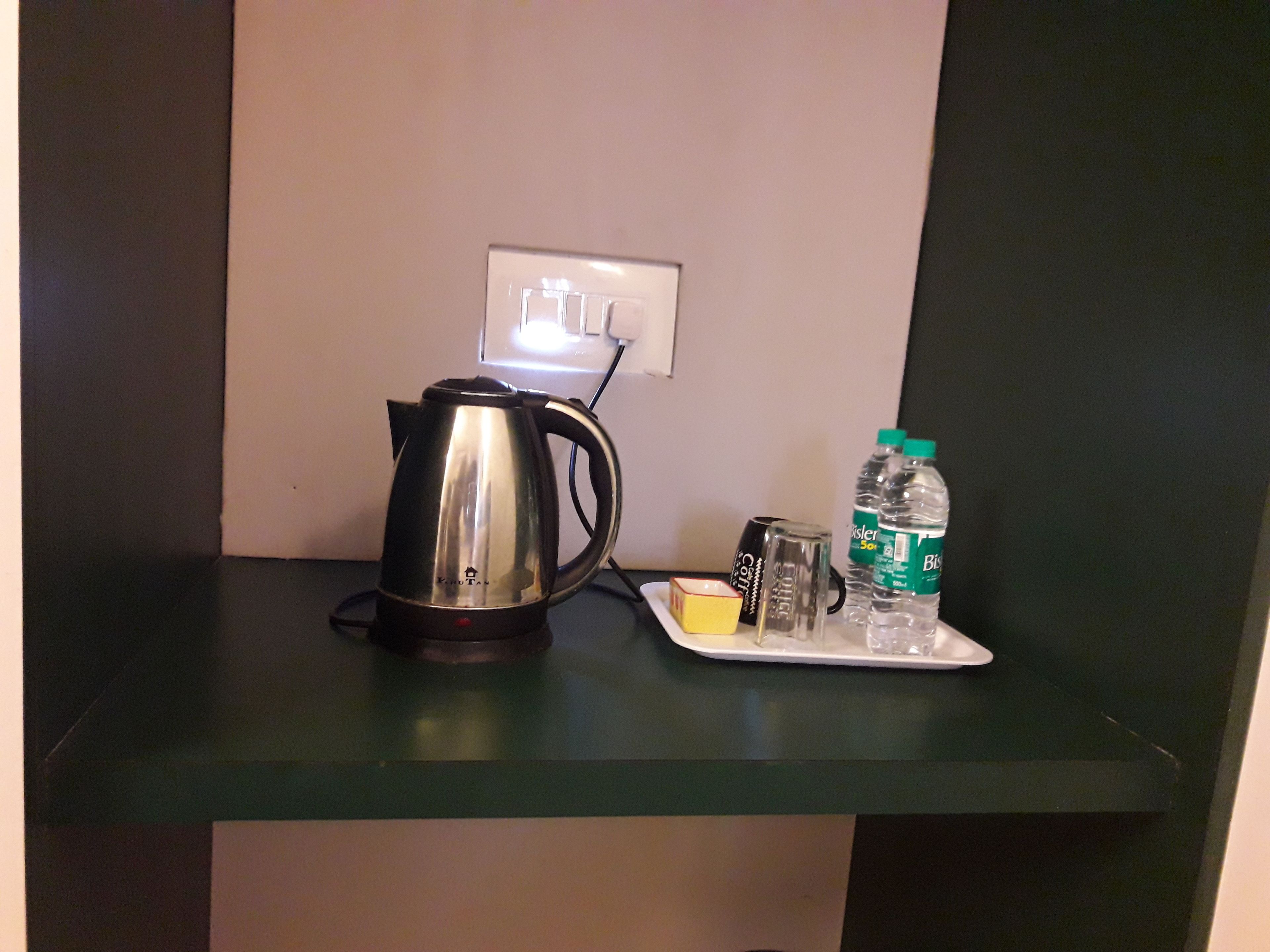 A kitchenette with a kettle, a plate with condiments, and two water bottles on a green countertop.