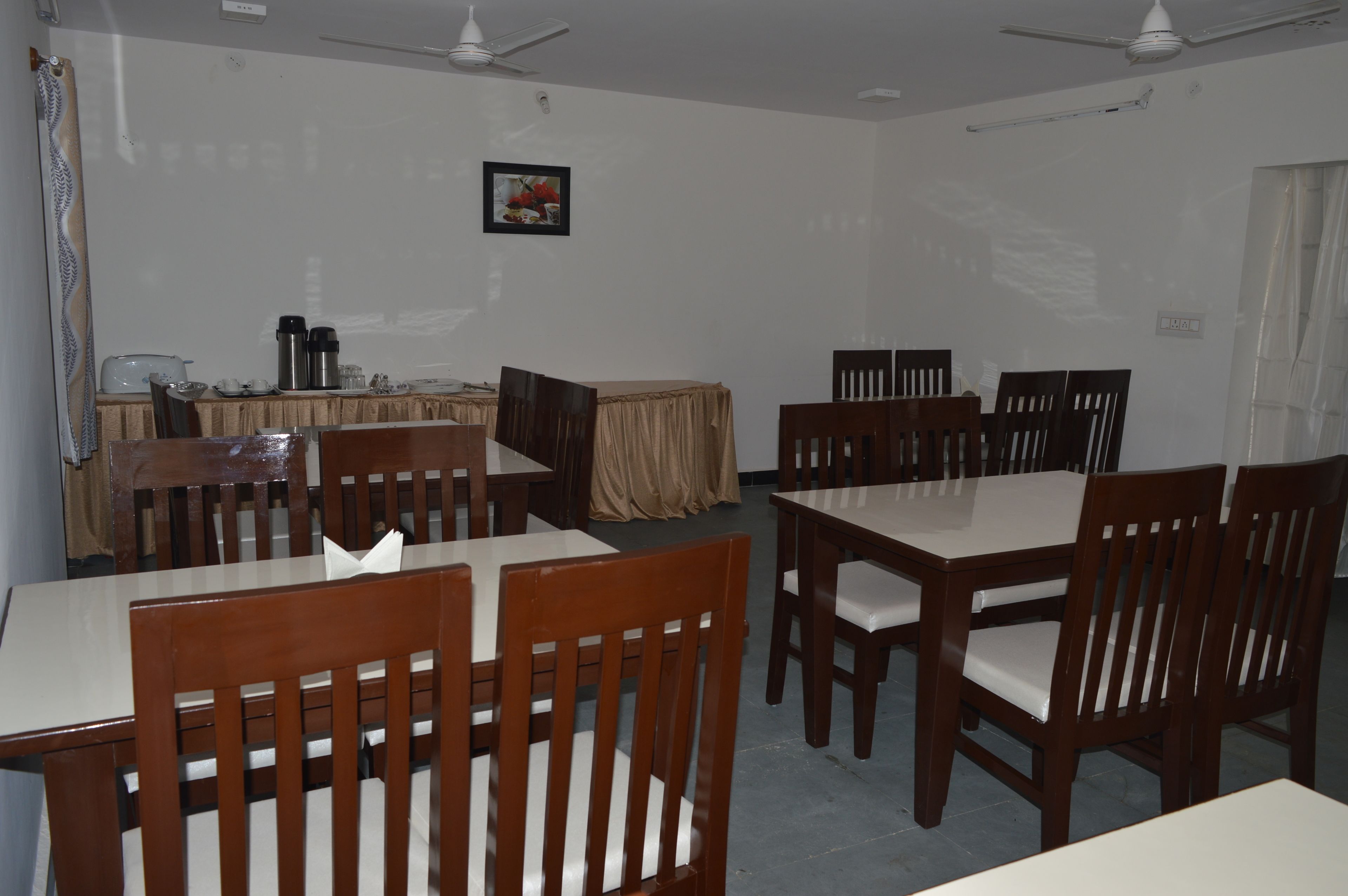 Un espace repas avec des tables et des chaises en bois, un ventilateur de plafond et une table sur laquelle se trouvent une machine à café et des tasses.