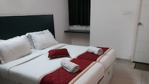 Una cama bien hecha con ropa de cama blanca y roja, un cabecero oscuro y una pequeña estantería encima.