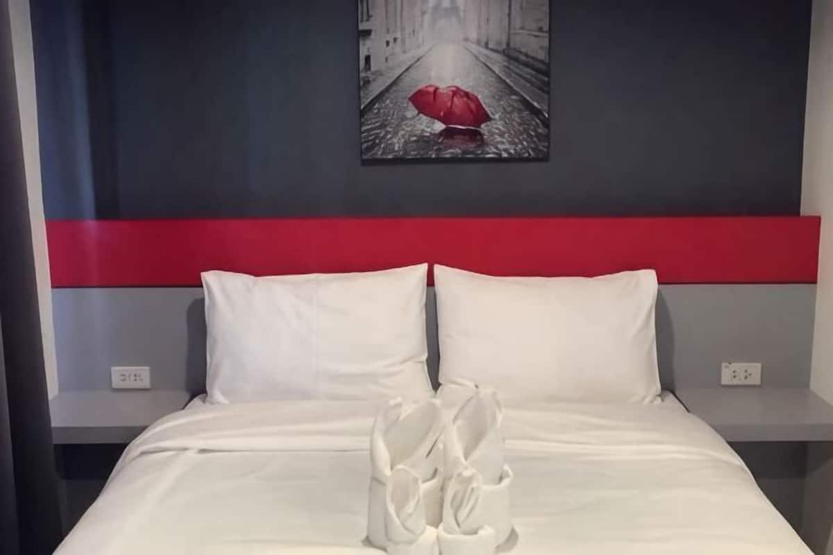 Un lit bien fait, avec une literie blanche, un mur d’accent rouge et un tableau encadré au-dessus.