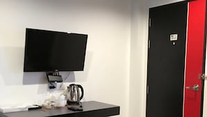 Une chambre moderne avec un bureau noir, un téléviseur fixé au mur, une porte rouge et une poubelle.