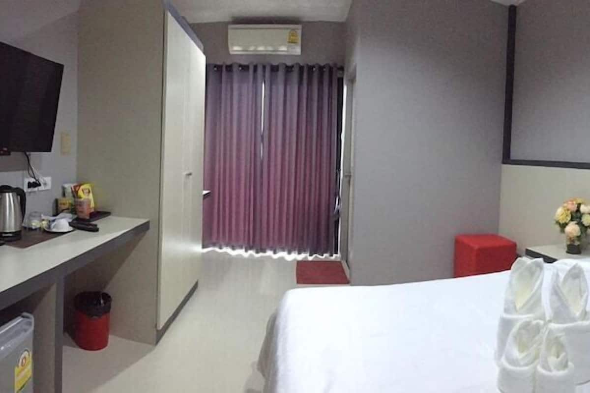 Une chambre d’hôtel avec un lit, une télévision, un bureau avec une bouilloire, une poubelle et un tabouret rouge.