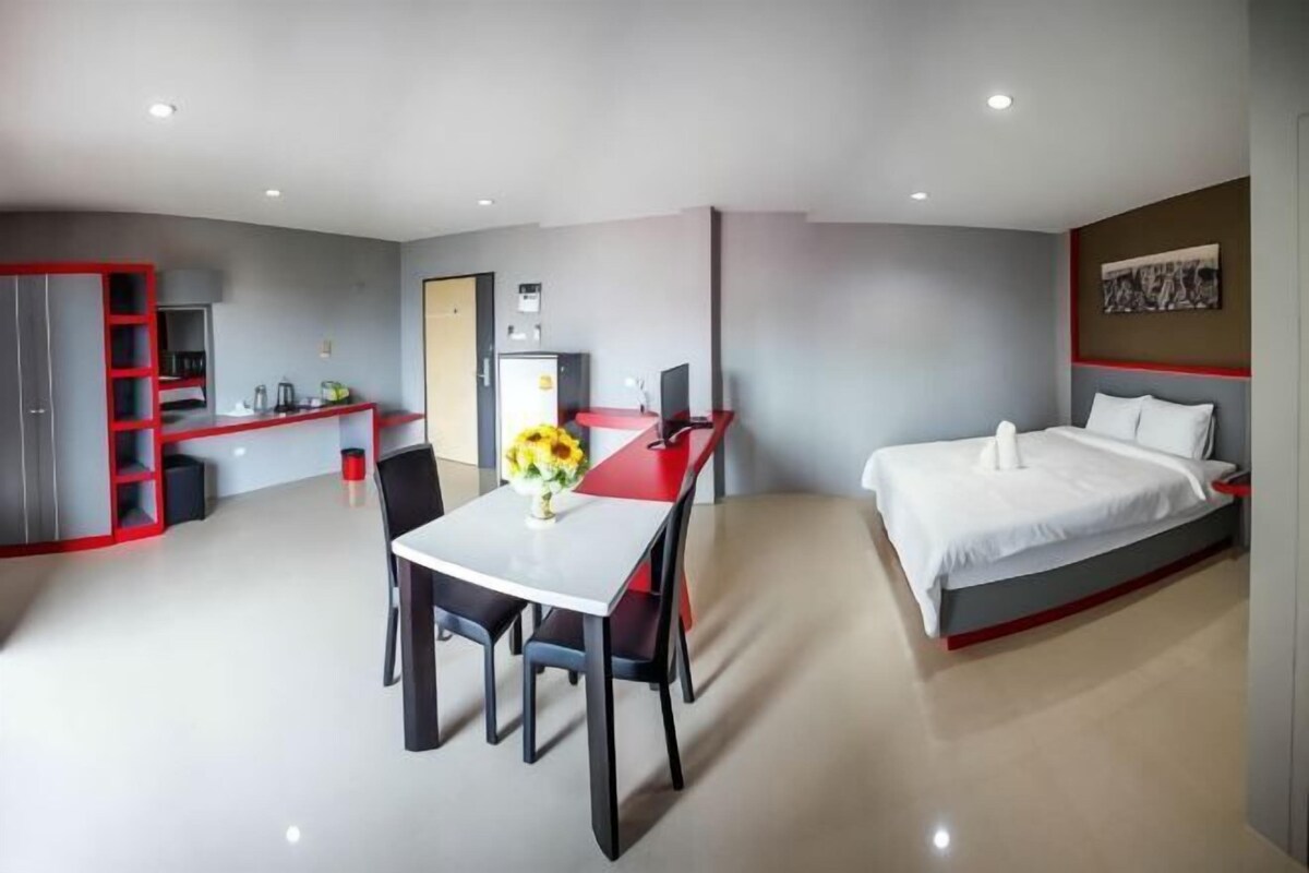 Een moderne hotelkamer met een bed, een eettafel met stoelen, een kitchenette en een garderobe met rode lijst.